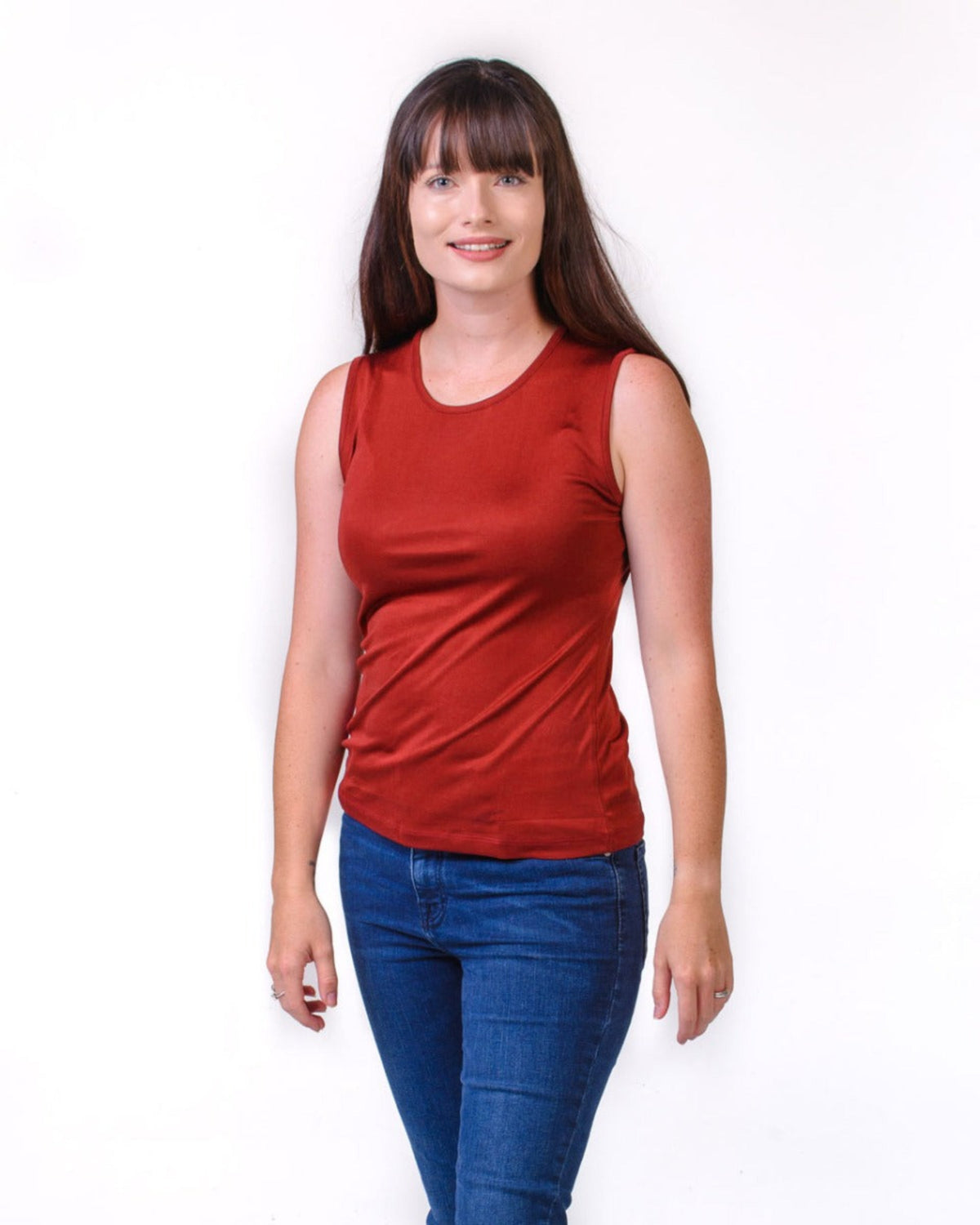 Woman wearing a silk red sleeveless top and blue jeans on a white background