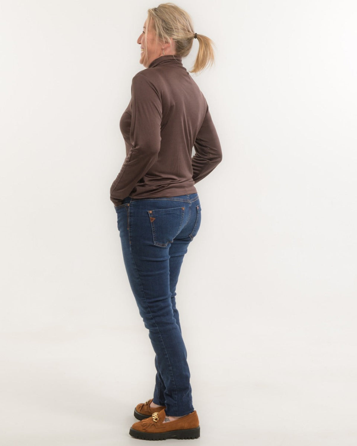 Person wearing a silk  brown long-sleeve top and blue jeans on a white background