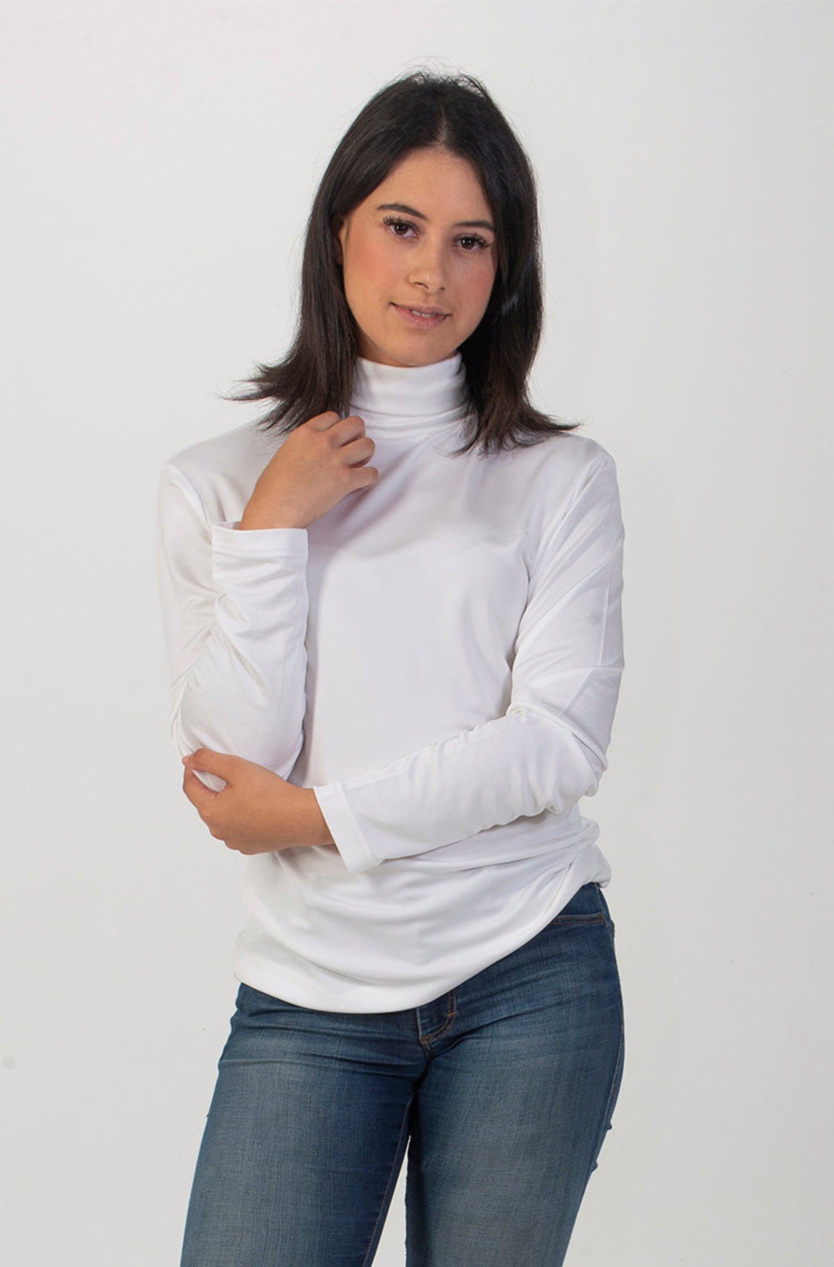 Woman wearing a silk white turtleneck sweater and blue jeans on a white background