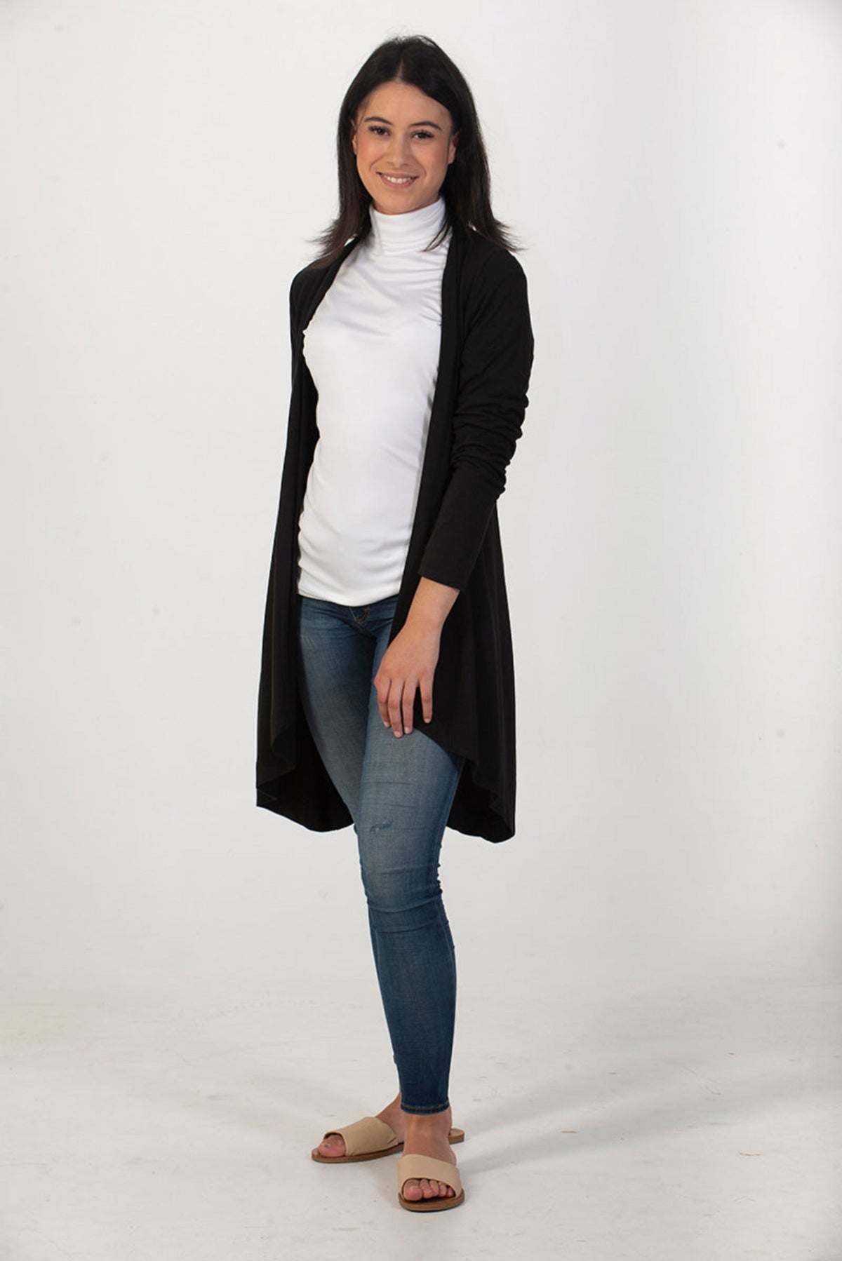 Woman wearing a black cardigan,silk  white turtleneck, and blue jeans on a white background