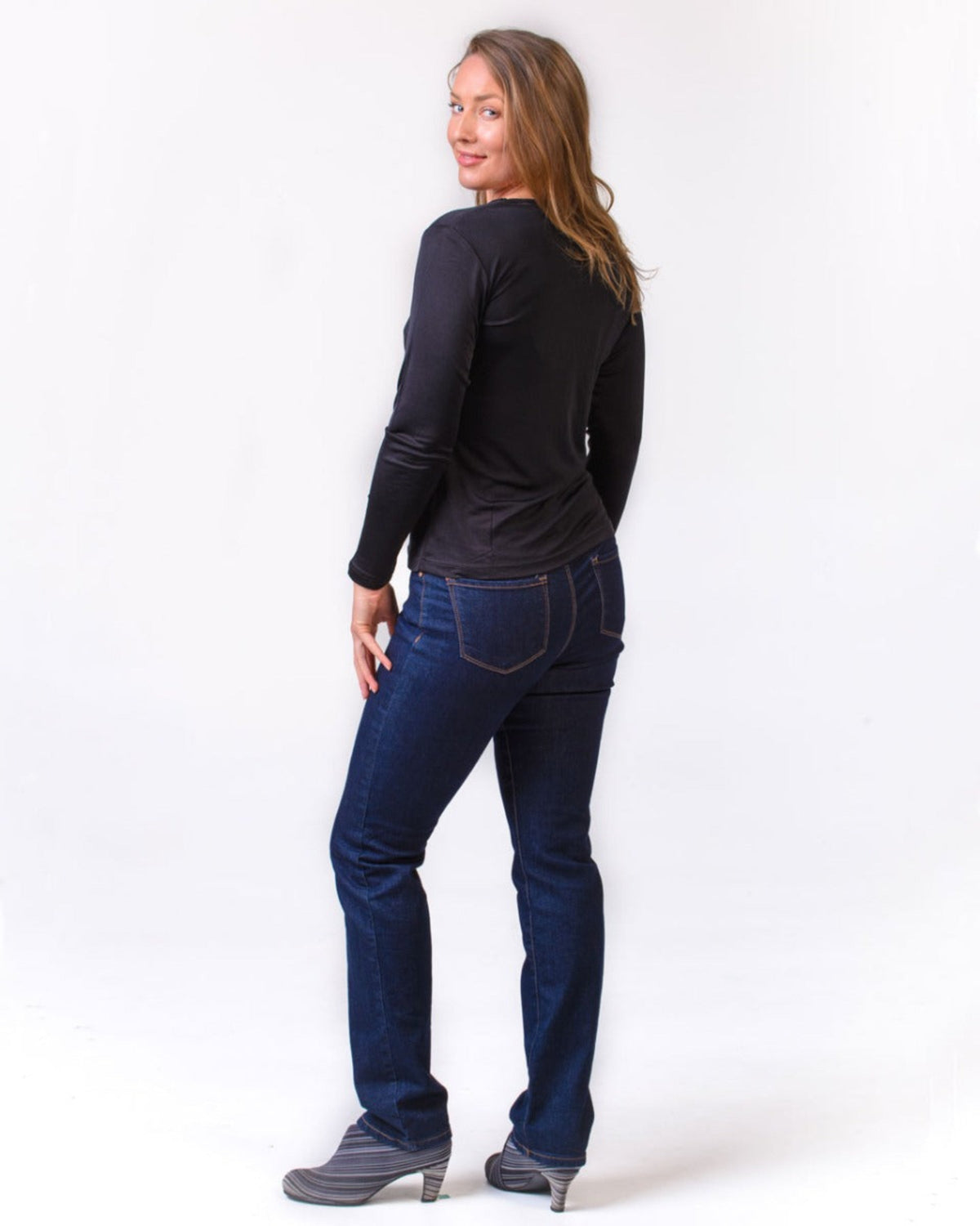 Woman wearing a silk  black long-sleeve top and blue jeans on a white background