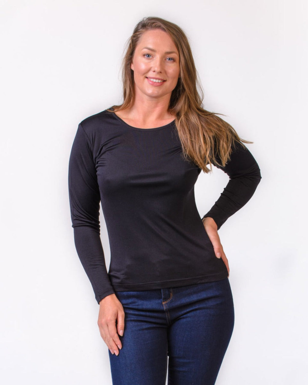Woman wearing a silk black long-sleeve top and blue jeans against a white background