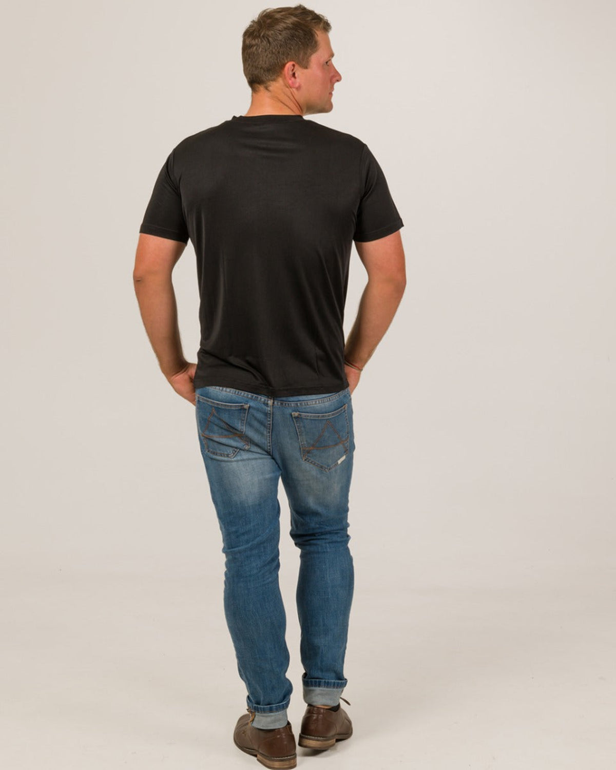 Man wearing a black silk vee neck t-shirt and blue jeans on a plain background