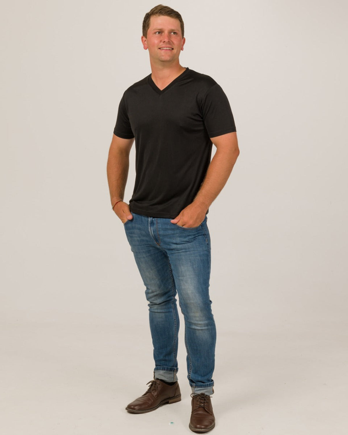 Man wearing a silk black t-shirt and blue jeans on a plain background