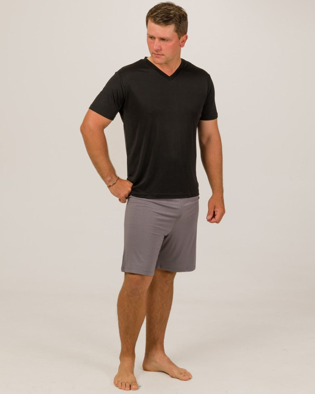 Man wearing a silk black t-shirt and gray shorts on a white background
