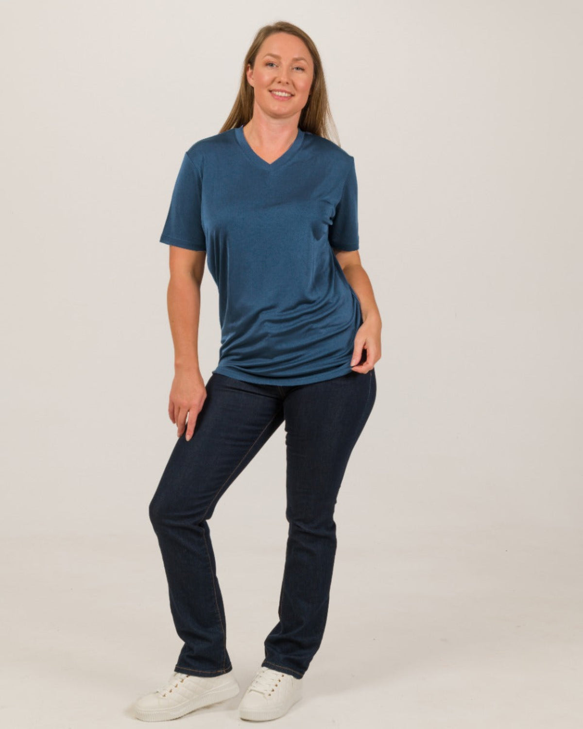 Woman wearing a blue silk vee neck t-shirt and dark pants on a white background