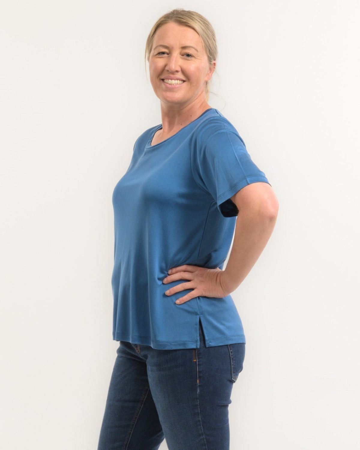 Woman wearing a silk blue t-shirt and jeans against a white background