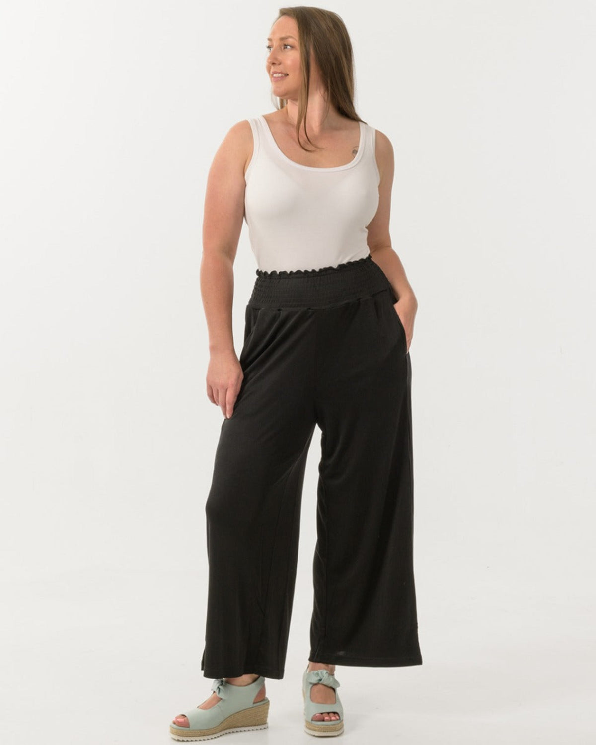 Woman wearing a white sleeveless top and silk  black wide-leg pants on a white background