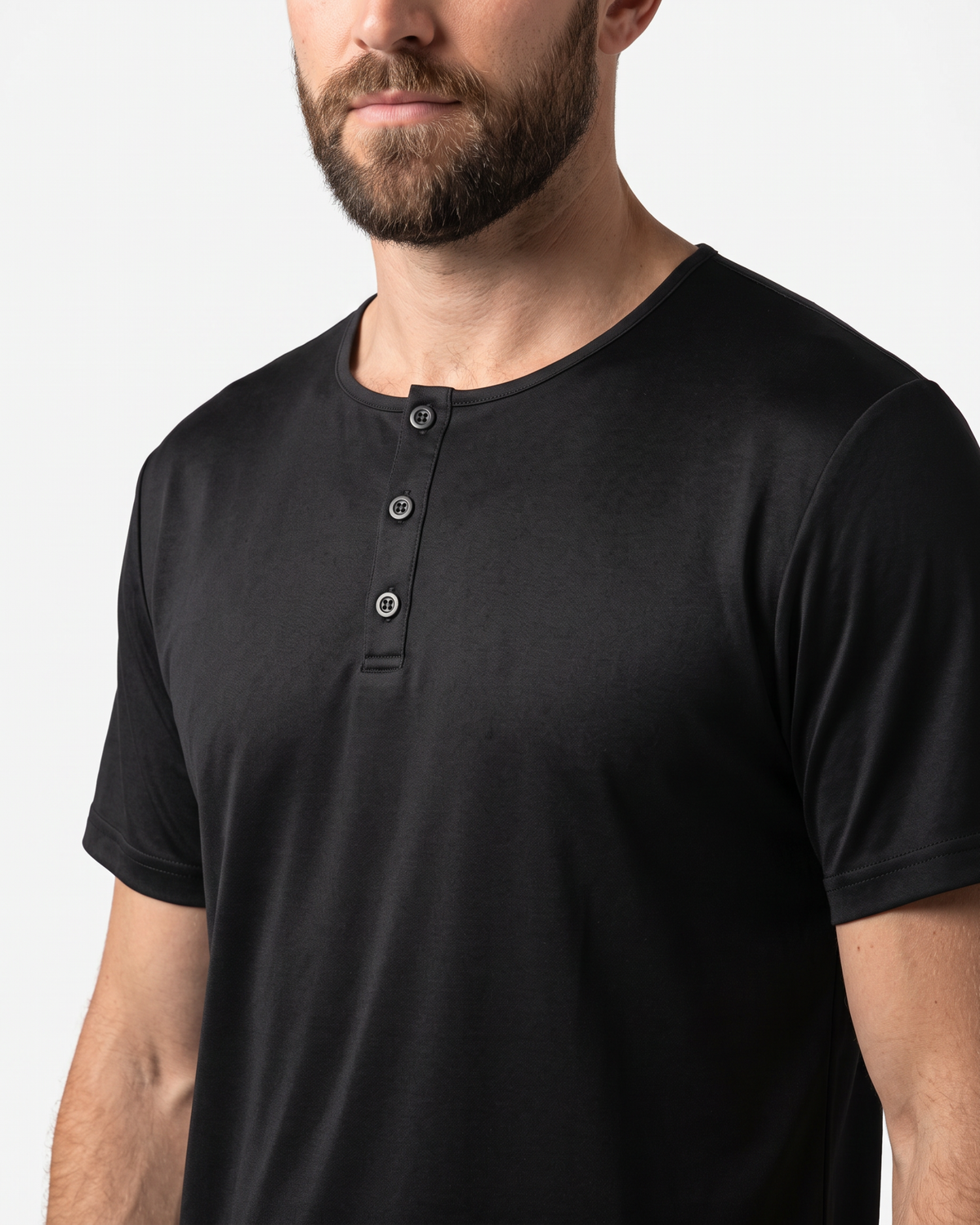 A close-up of a man wearing a black short-sleeve henley t-shirt with three buttons on the chest, set against a plain light background.