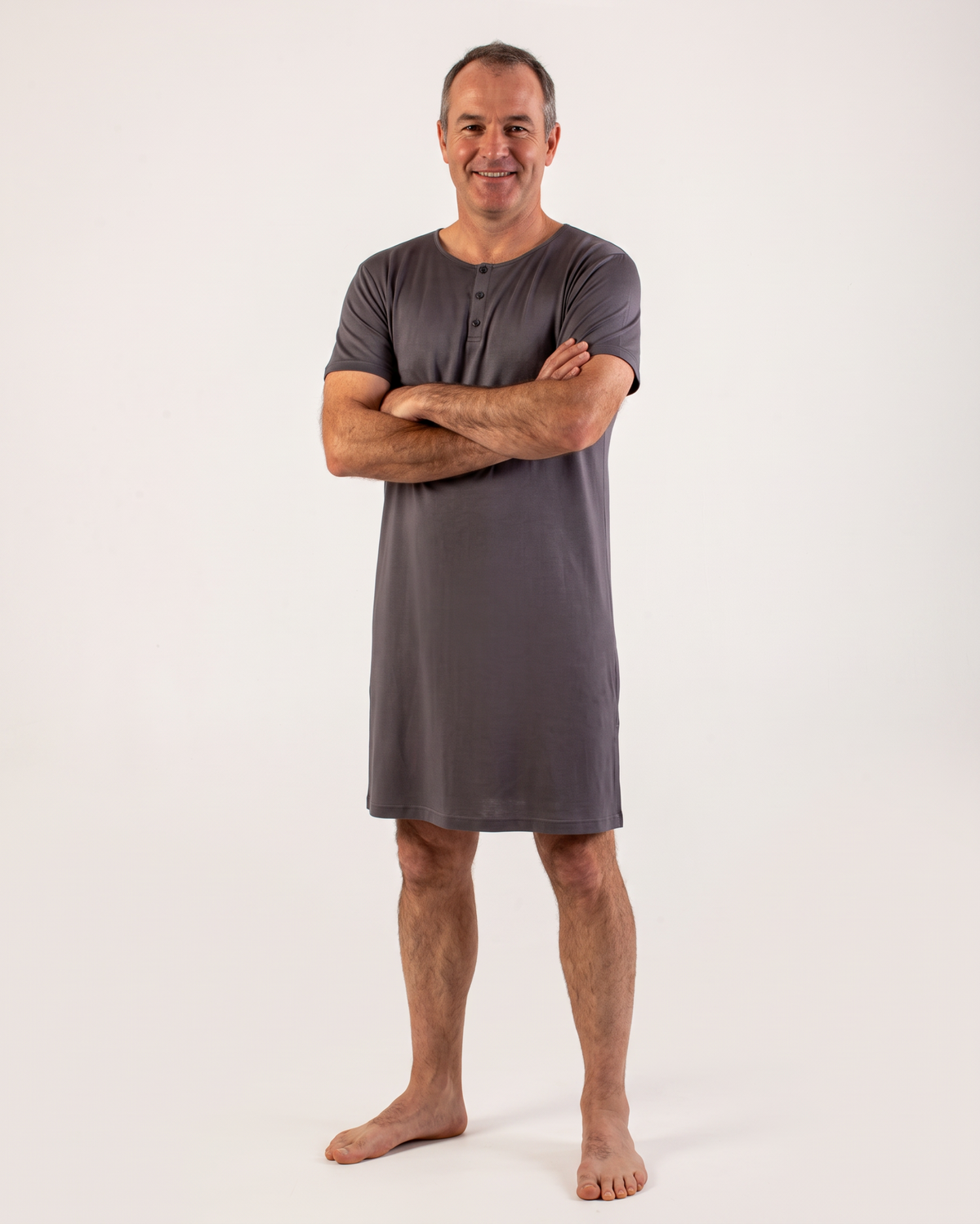 A man wearing a dark gray short-sleeve henley nightshirt, standing with arms crossed against a plain white studio background.