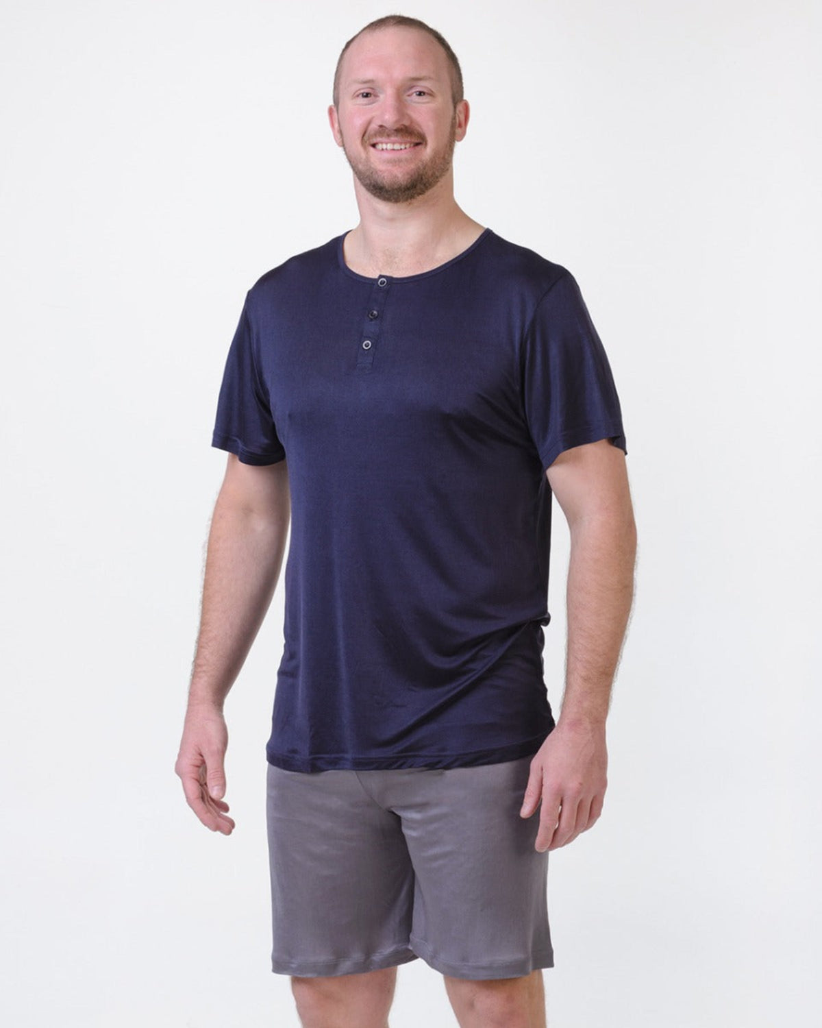 Man wearing a silk  navy blue henley shirt and gray shorts on a white background