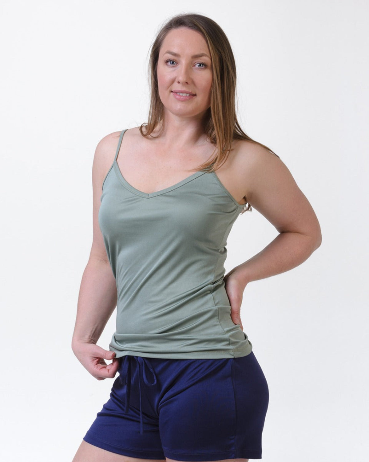 Woman wearing a sage green silk camisole  tank top and blue shorts on a white background