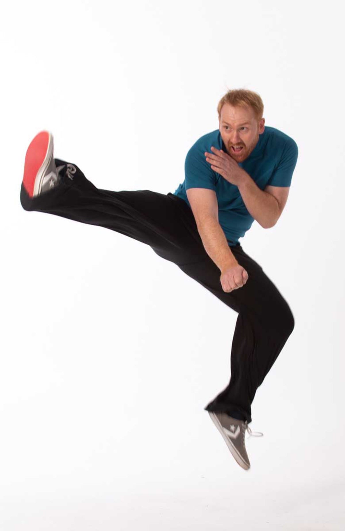 Man in bamboo leisure blue shirt and black pants kicking his leg up on a white background