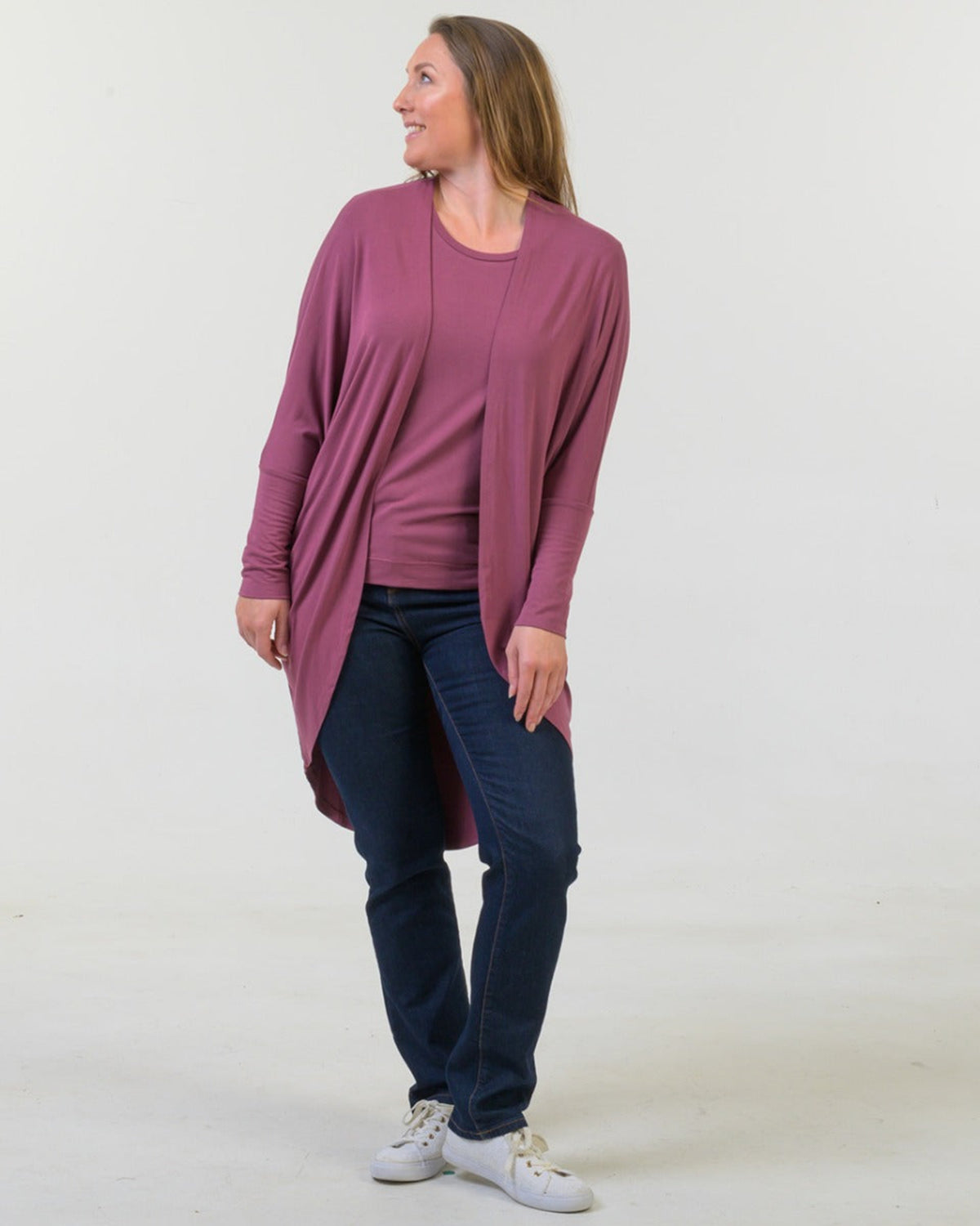 Woman bamboo cocoon wearing a long mauve cardigan over a dark top and jeans on a white background