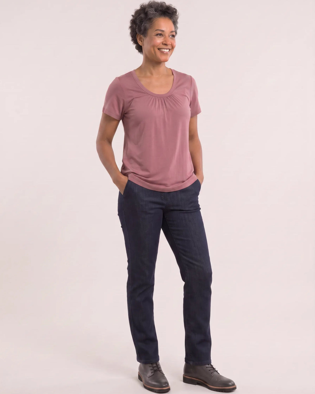 A woman modeling a dusty rose short-sleeve top and dark navy pants against a solid light beige studio background.