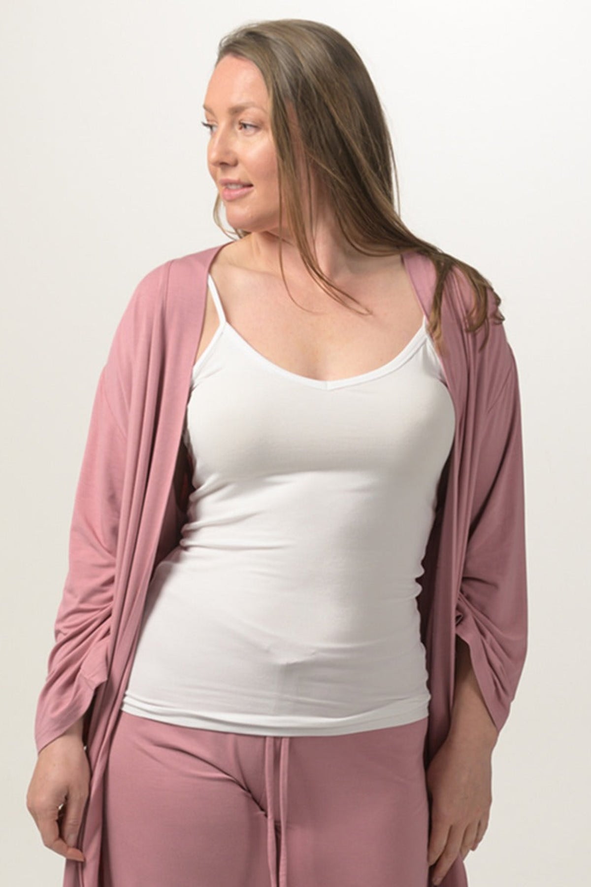 Woman wearing a pink cardigan, white tank top, and pink pants on a plain background