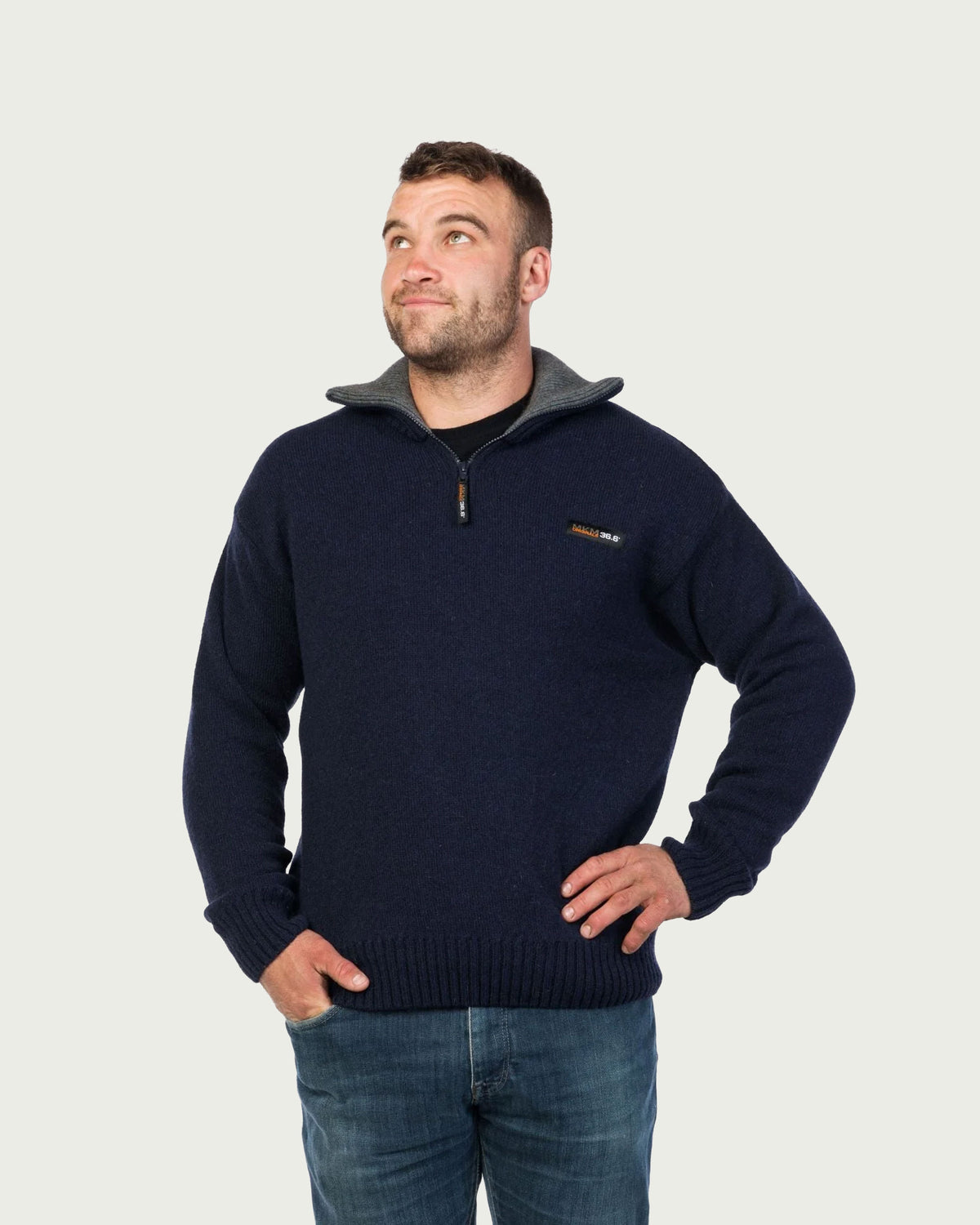 possum merino A man wearing a navy blue quarter-zip sweater with a gray hood, paired with blue jeans, standing against a light gray background.