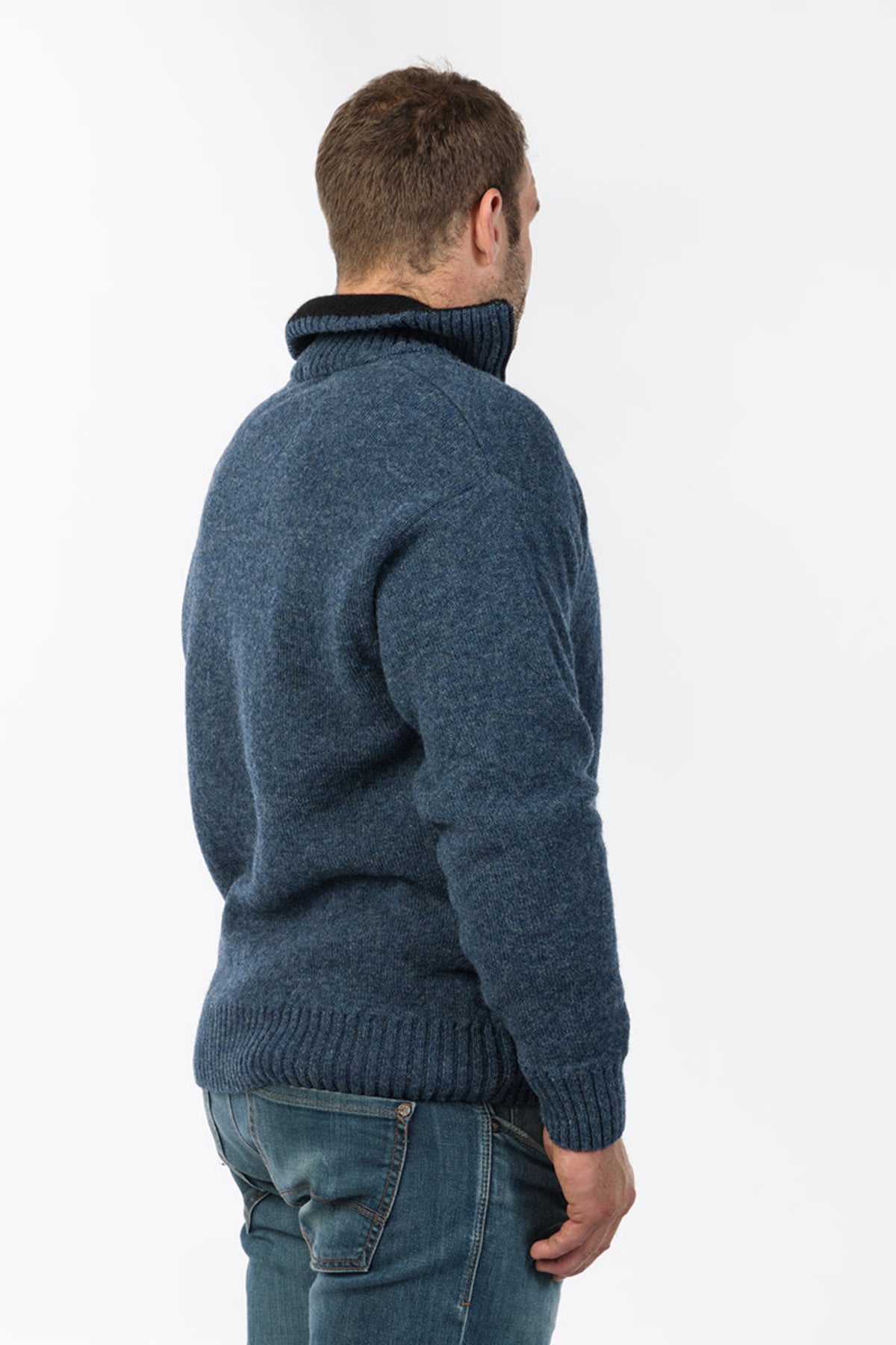 Possum Merino Man wearing a blue knitted sweater and jeans on a white background