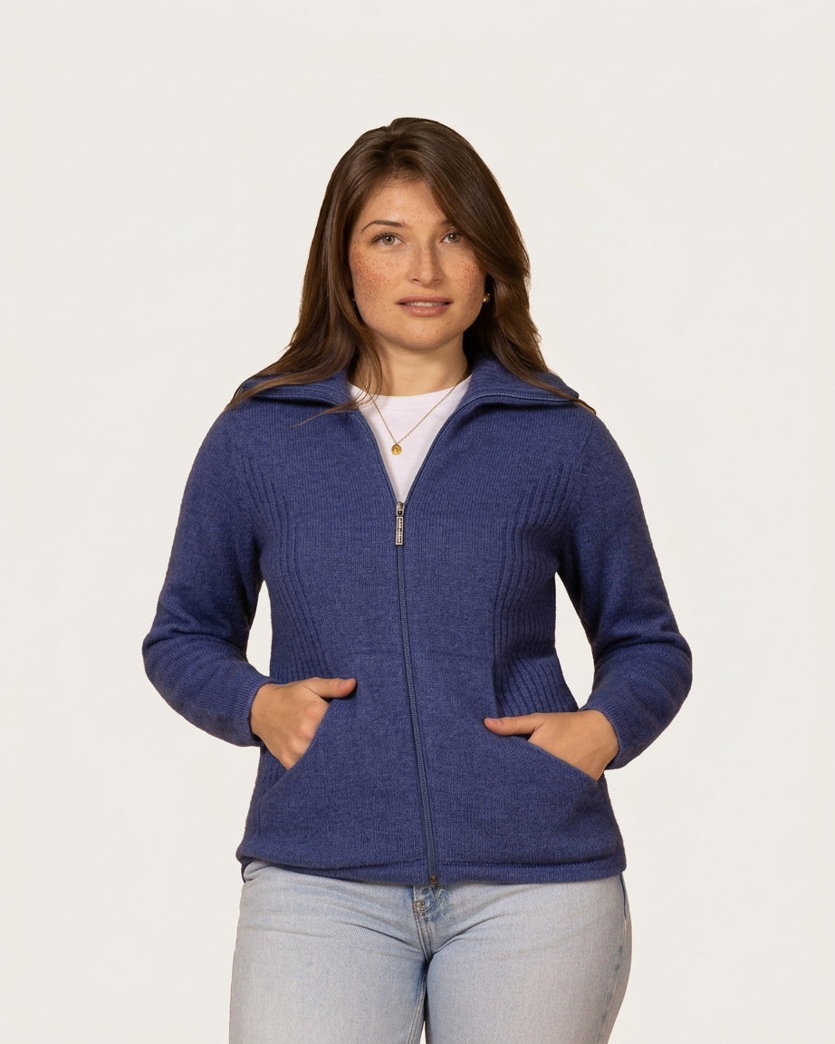 A woman modeling a heathered blue zip-up possum merino knit cardigan with a stand collar and front pockets, paired with a white top and light-wash jeans, against a solid off-white background.