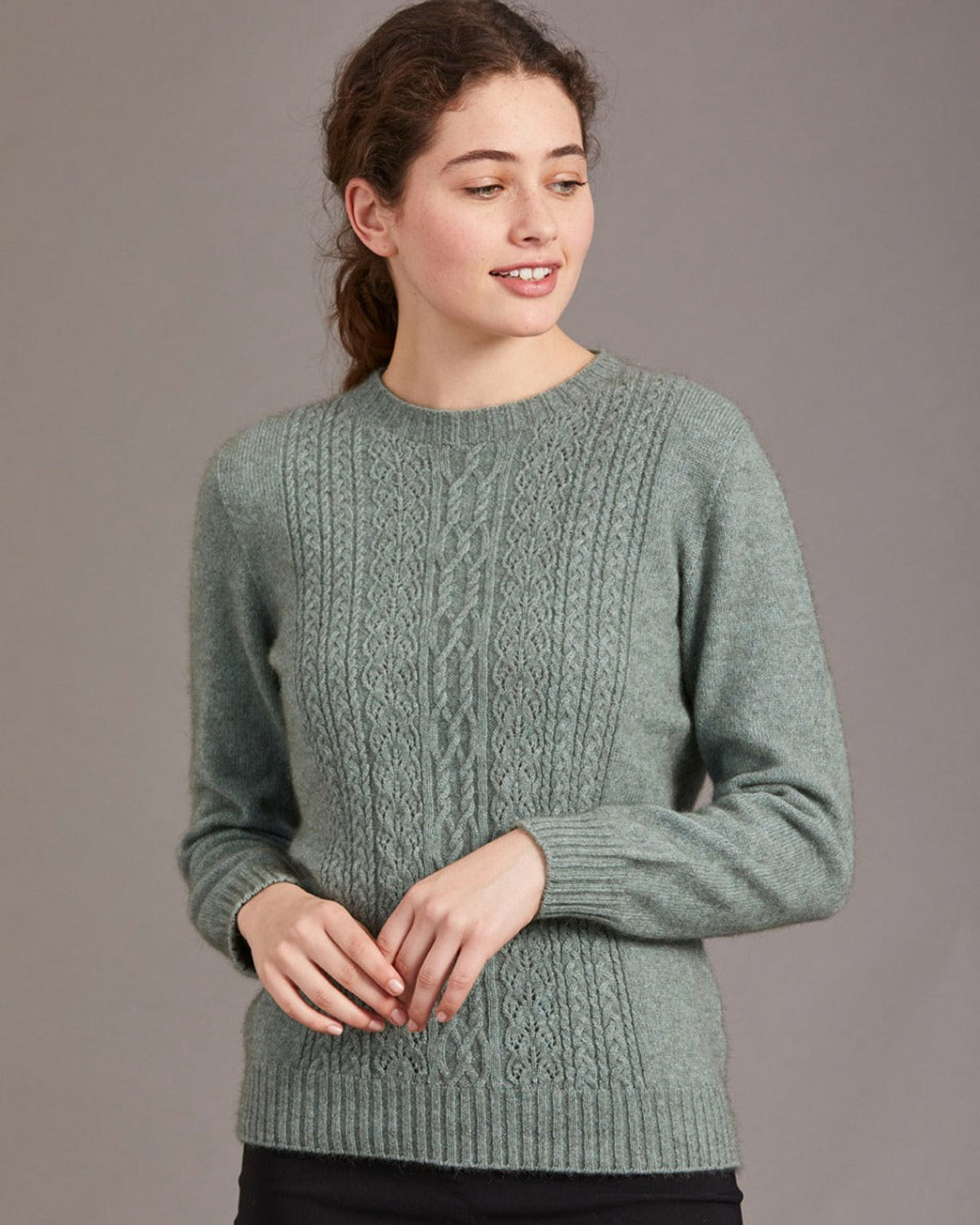 Woman wearing a green cable knit possum merino sweater against a plain background