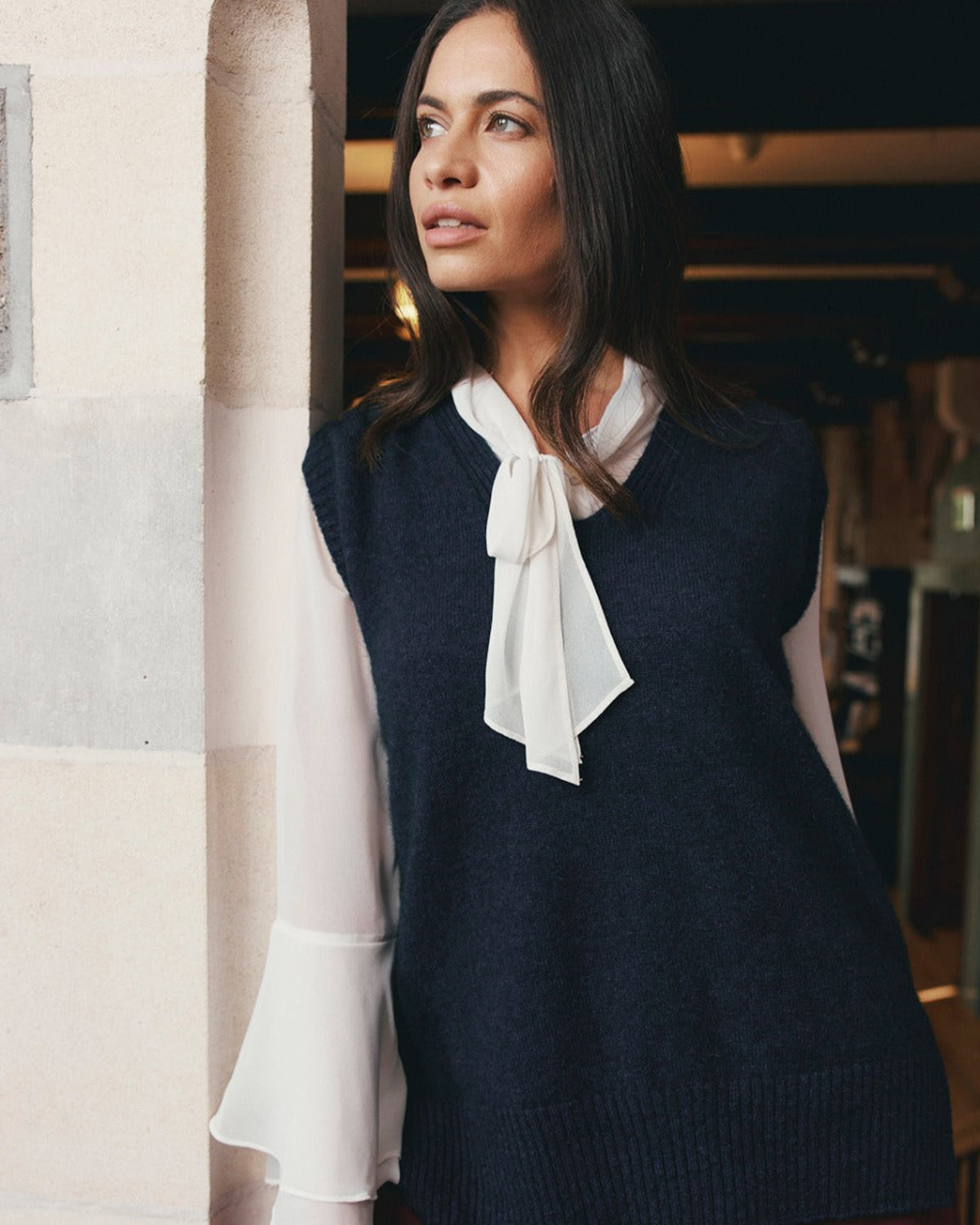 Possum merino Woman wearing a navy dress with a white blouse and sheer sleeves in an indoor setting.