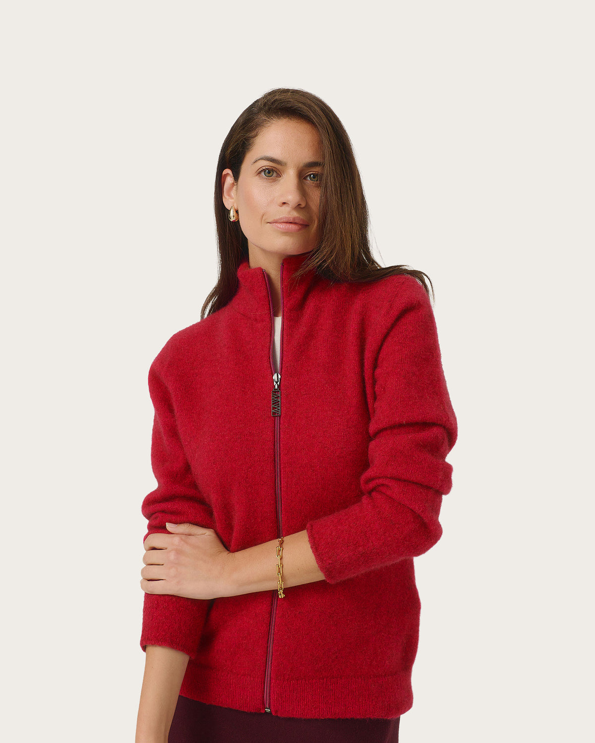 A woman wearing a bright red possum merino zip-up jacket with a stand collar, photographed against a plain light gray studio background.
