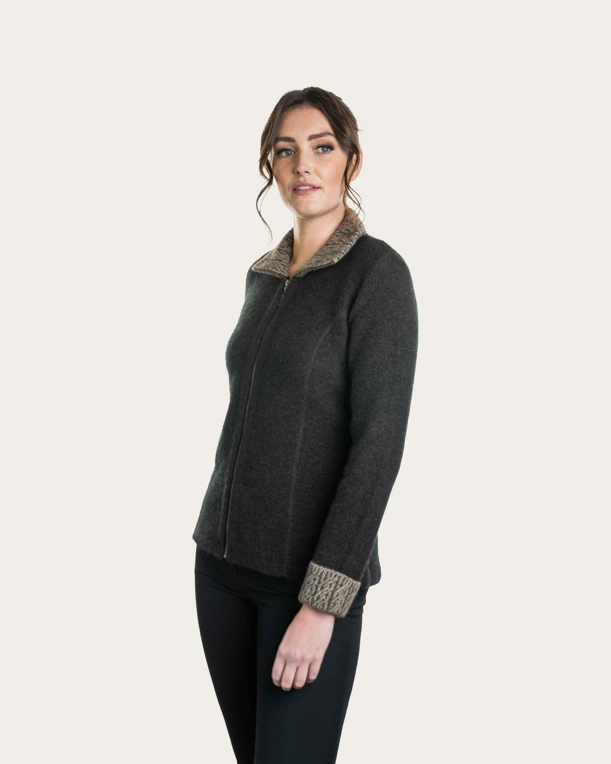 A woman modeling a dark espresso brown, possum merino zip-up jacket with a textured beige sherpa collar and matching knit cuffs, paired with black pants, against a solid off-white background.