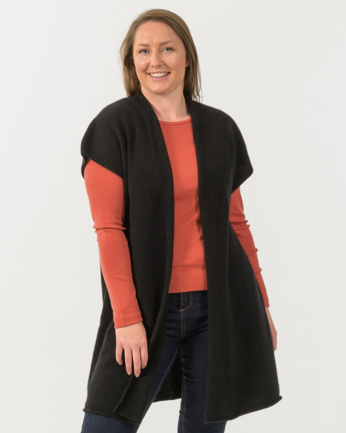 Possum merino gilet Woman wearing a black cardigan over an orange shirt on a white background