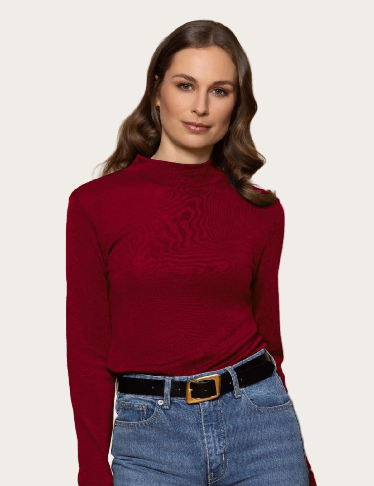 Woman wearing a merino red sweater and blue jeans against a beige background