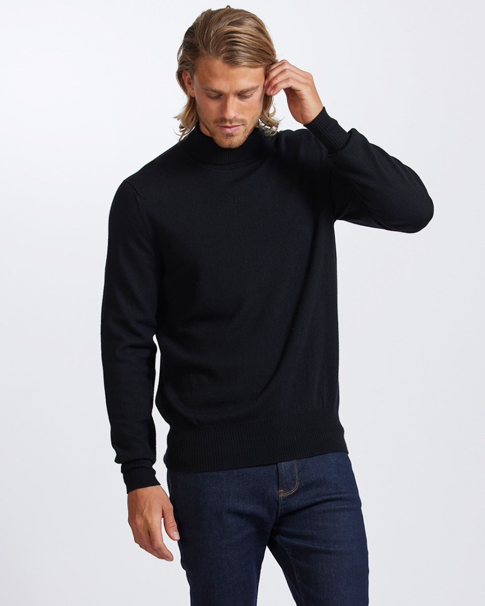 Man wearing a merino black turtleneck sweater and blue jeans on a white background