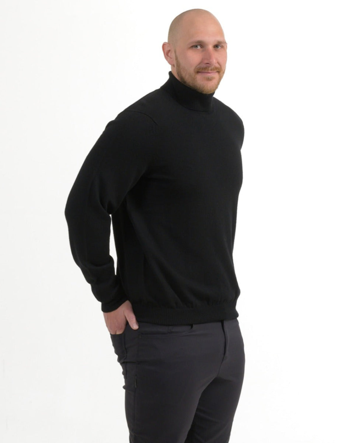 Man wearing a merino black turtleneck sweater and dark pants on a white background