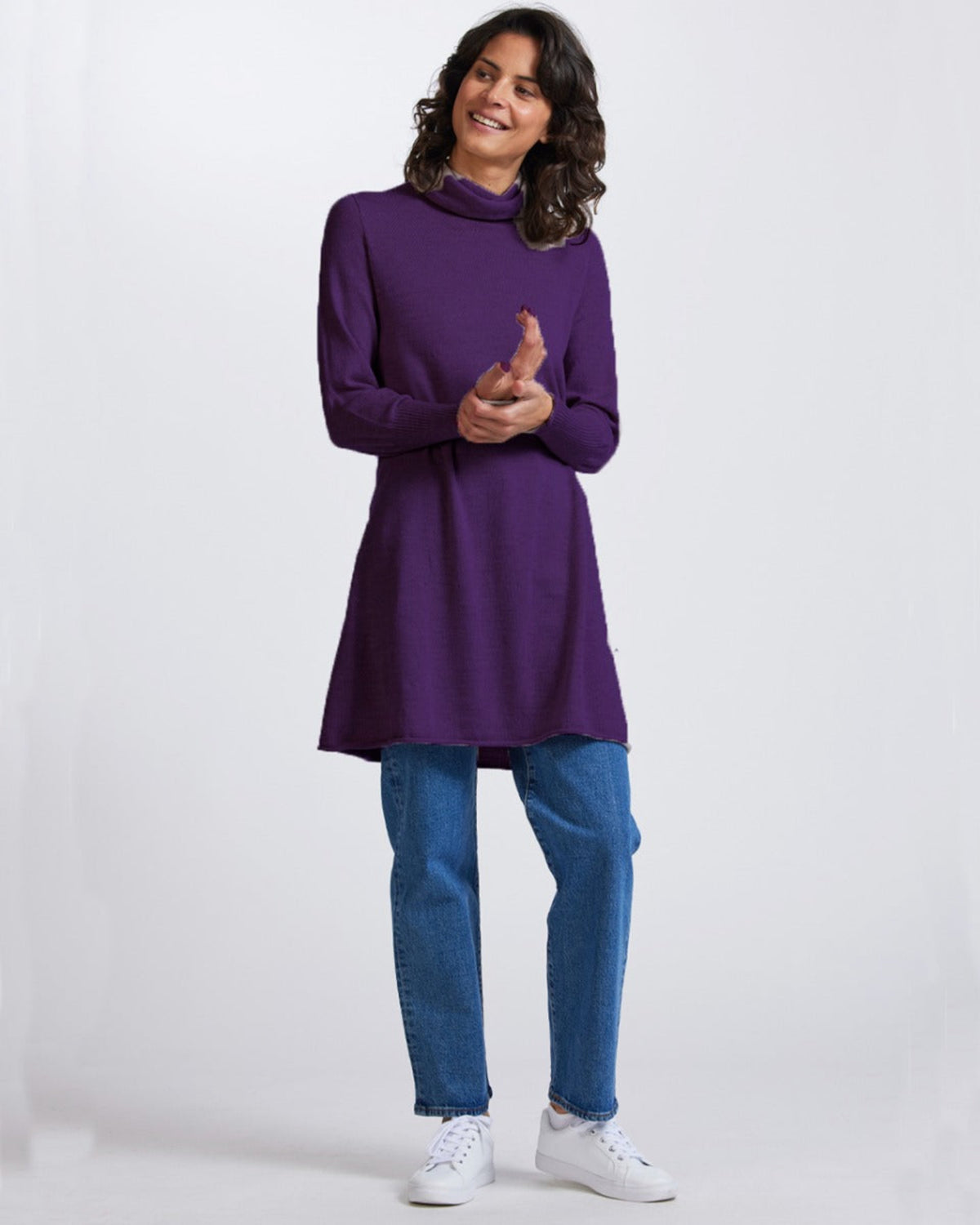 Woman wearing a merino purple tunic and blue jeans on a white background