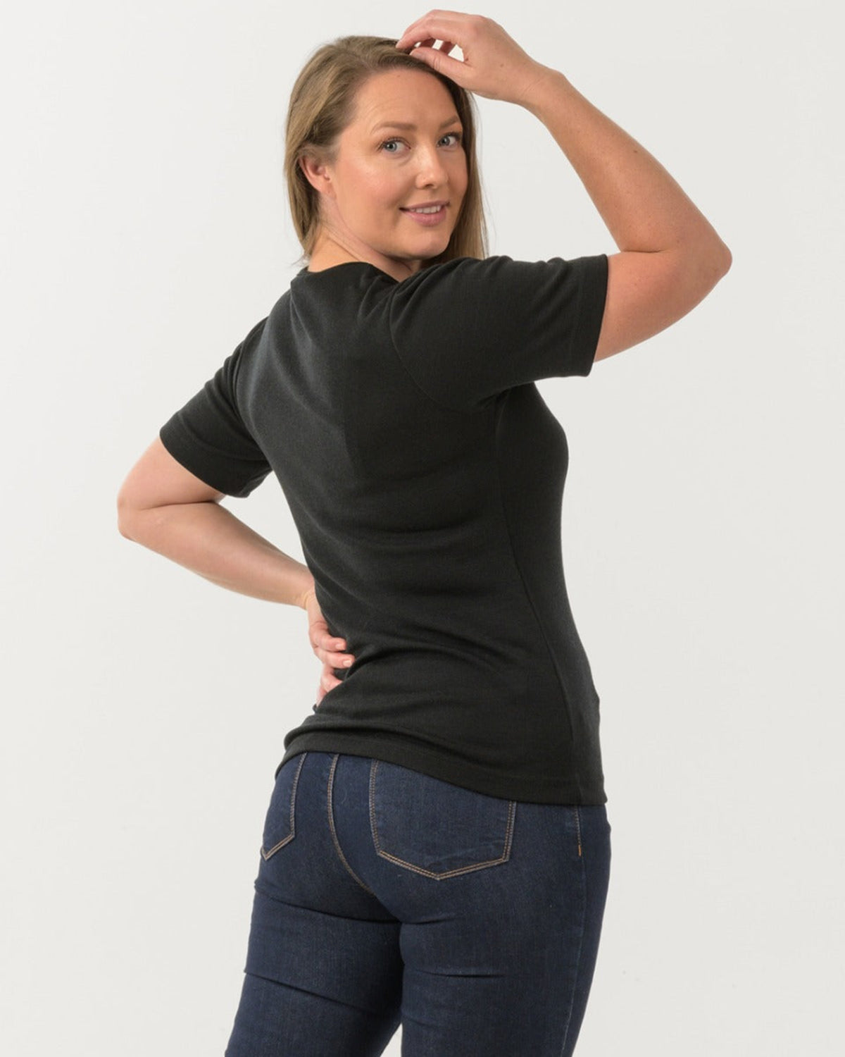 Woman wearing a merino black t-shirt and blue jeans on a white background