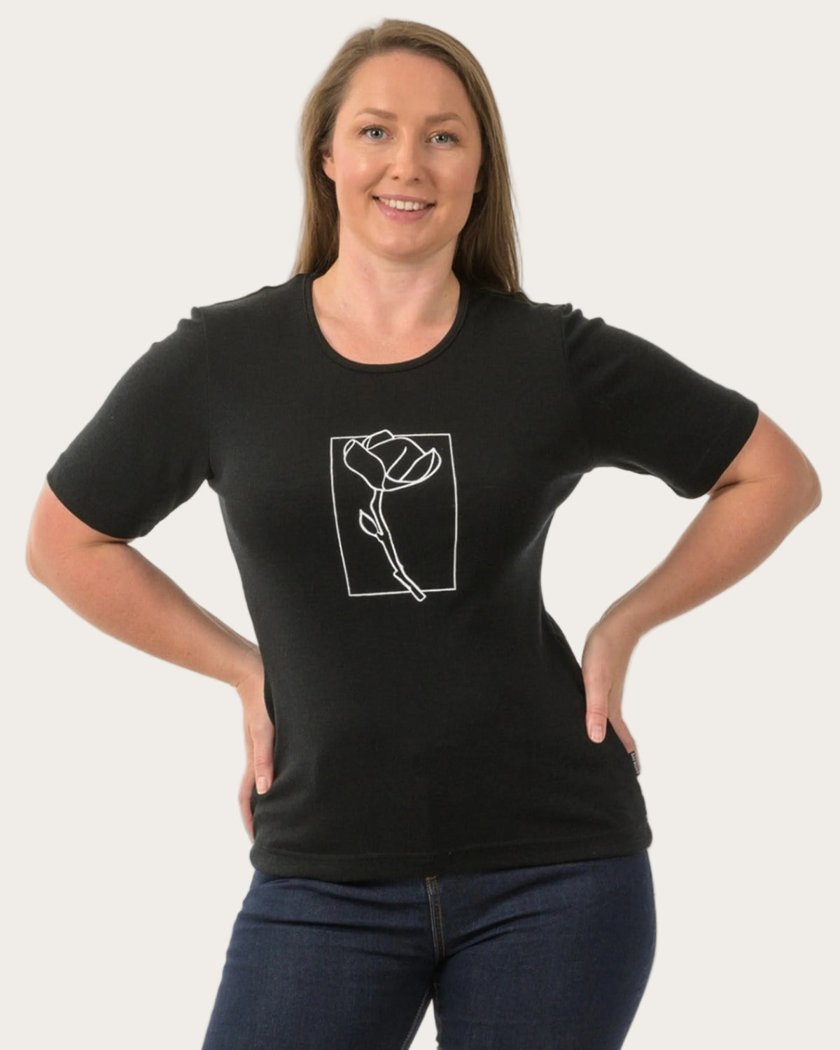 Woman wearing a merino black t-shirt with a white graphic design on a plain background