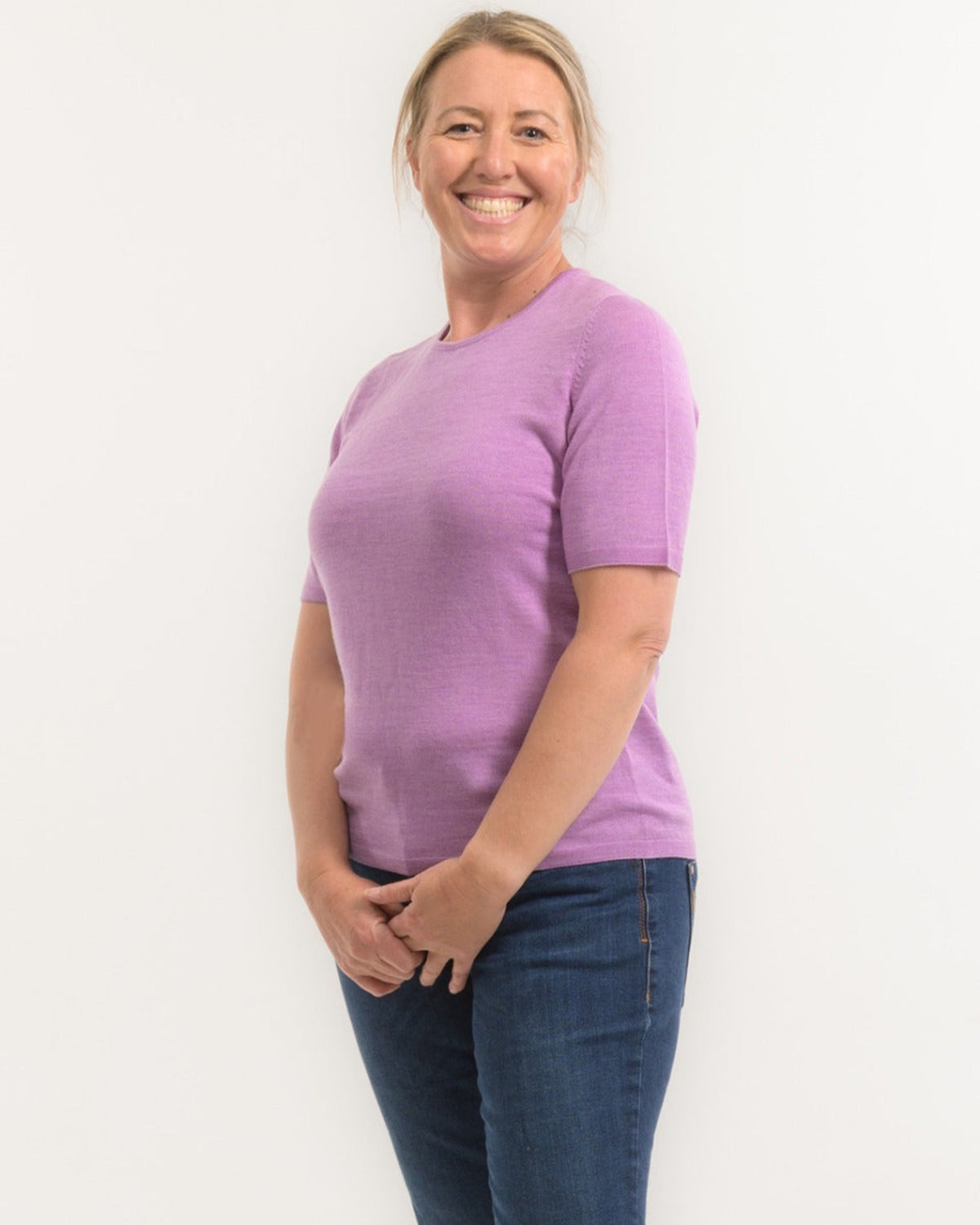 Woman wearing a merino purple shirt and blue jeans on a white background