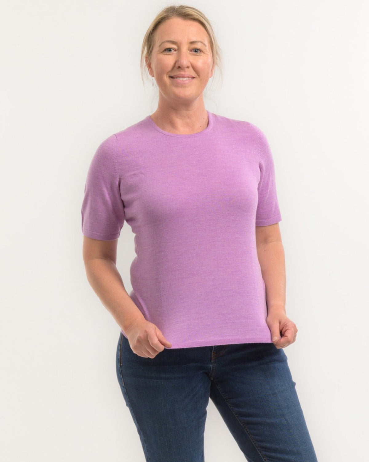 Woman wearing a merino purple shirt and blue jeans on a white background