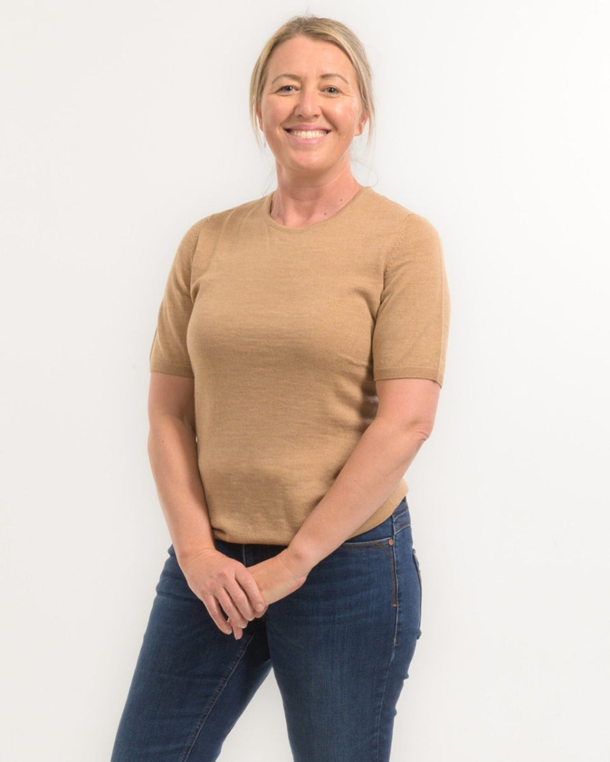 Woman wearing a merino beige sweater and blue jeans against a white background