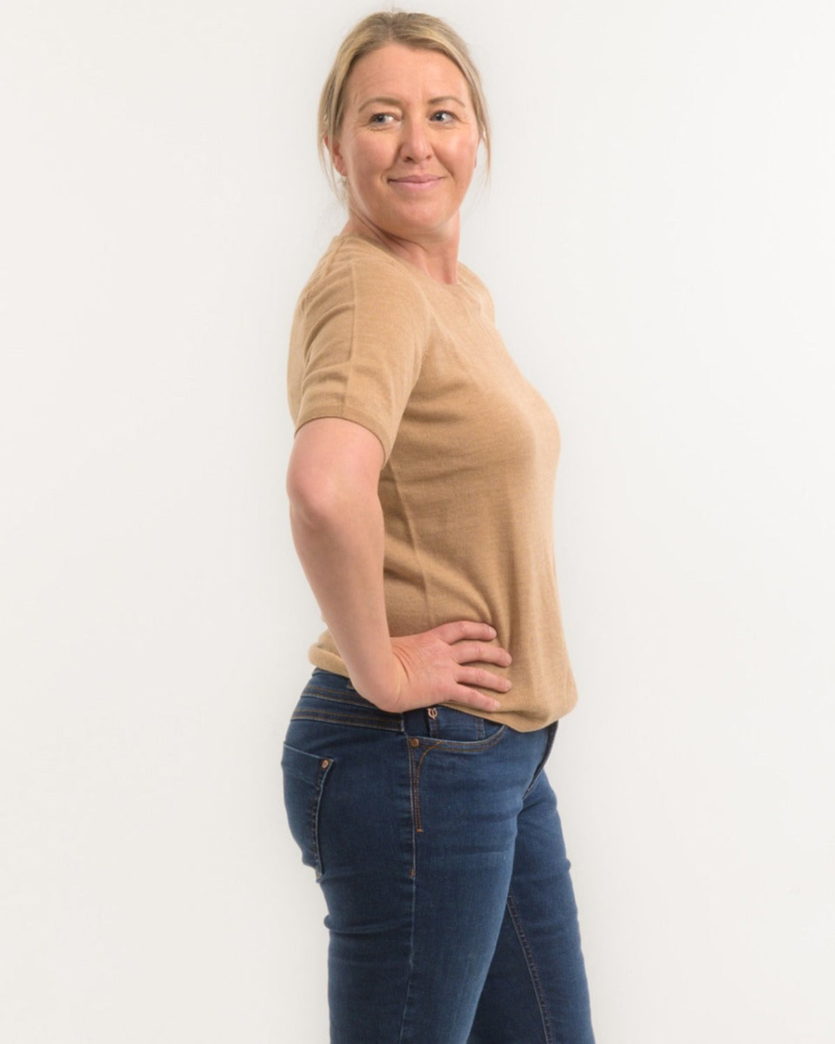 Woman wearing a merino beige sweater and blue jeans against a white background