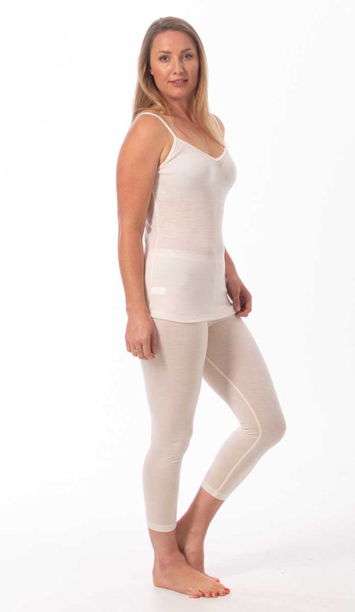 Woman wearing a merino  white tank top and beige leggings on a white background