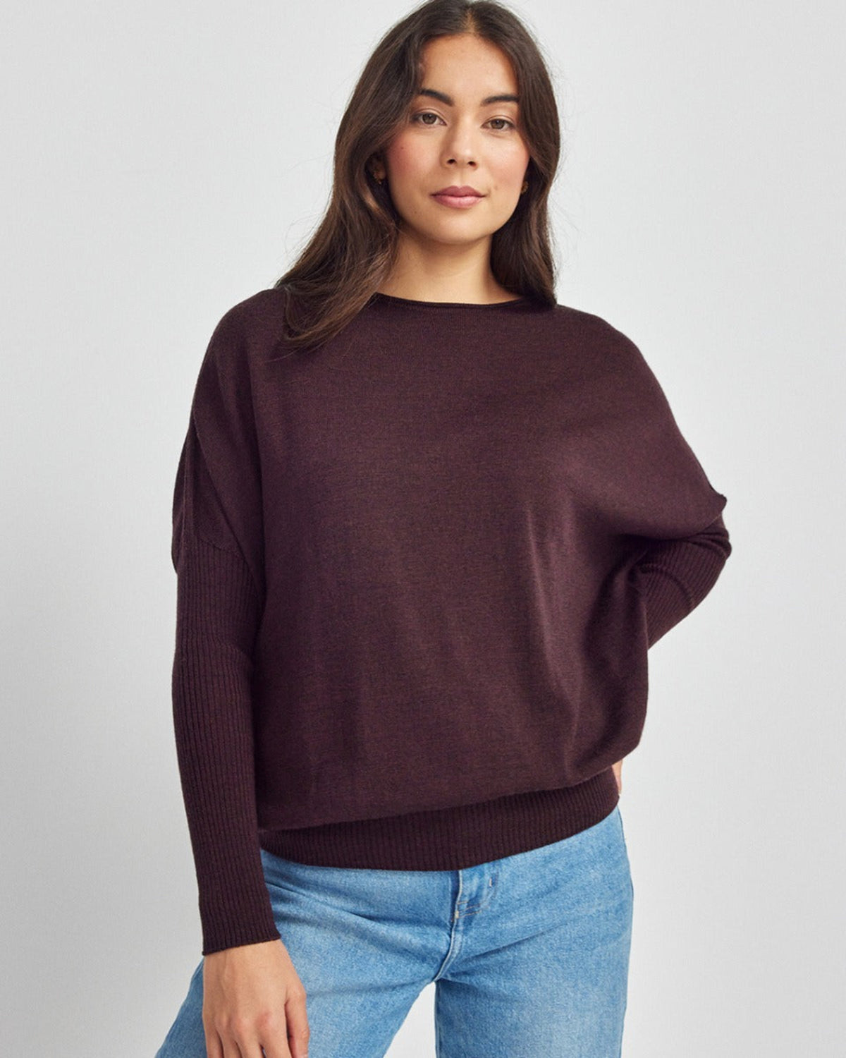 Woman wearing a merino dark brown sweater and blue jeans on a light gray background