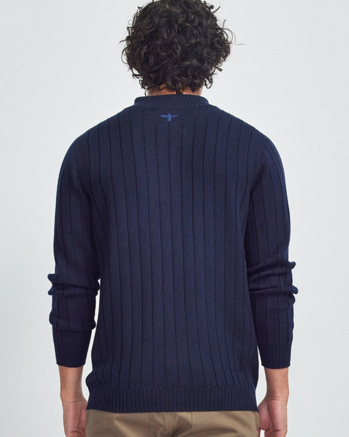 Person wearing a merino navy blue sweater with a visible brand logo on a light gray background