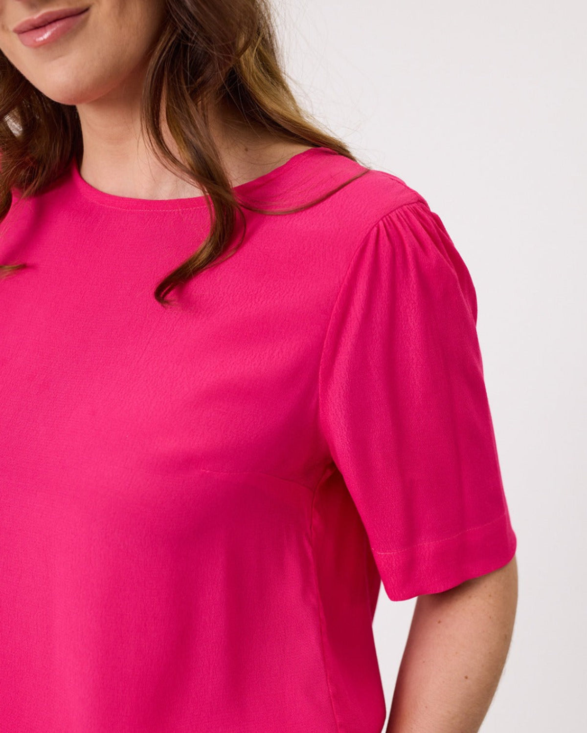 Close-up of a person wearing a bright pink top with puff sleeves on a white background