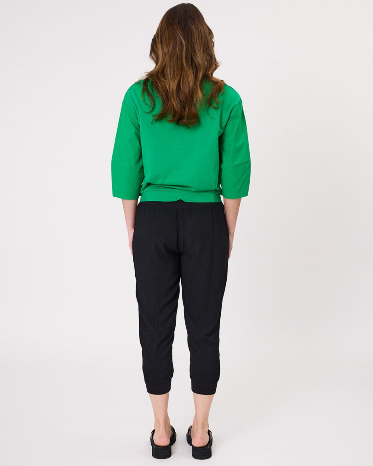 Person wearing a green top and black pants on a white background