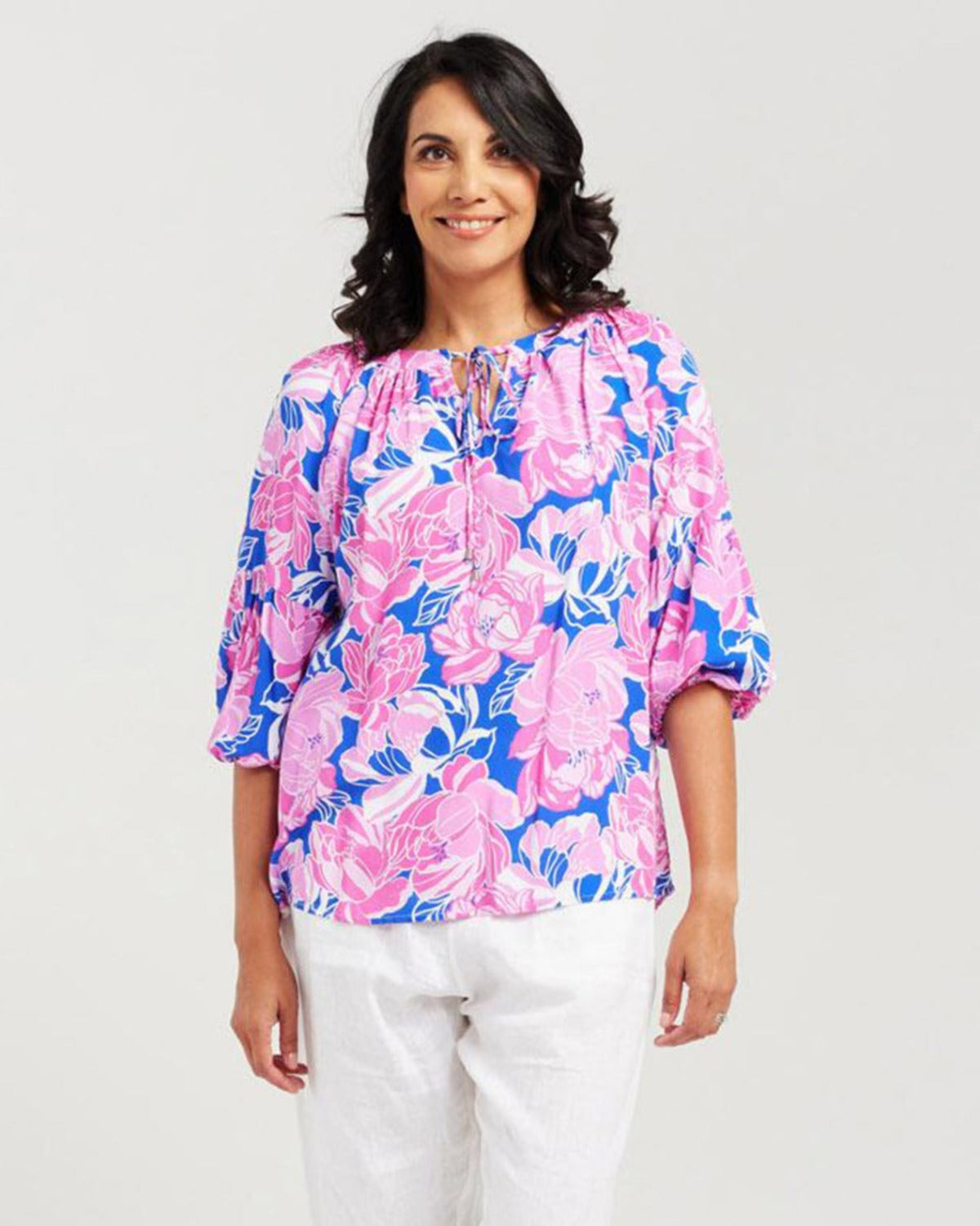 Woman wearing a colorful floral blouse with white pants on a light gray background