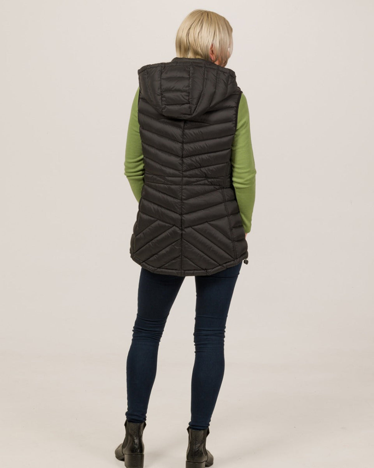 Person wearing a black quilted vest over a green long-sleeve shirt on a beige background