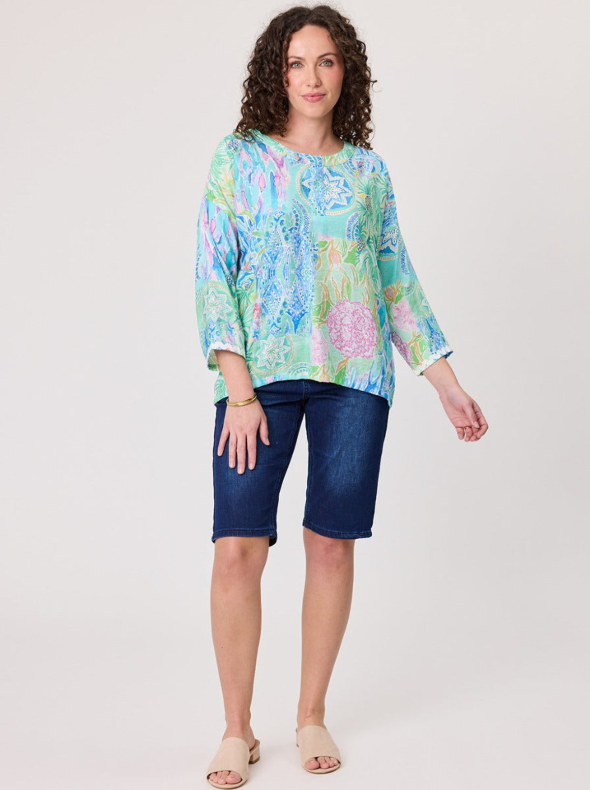 Woman wearing a colorful floral blouse and blue shorts on a white background