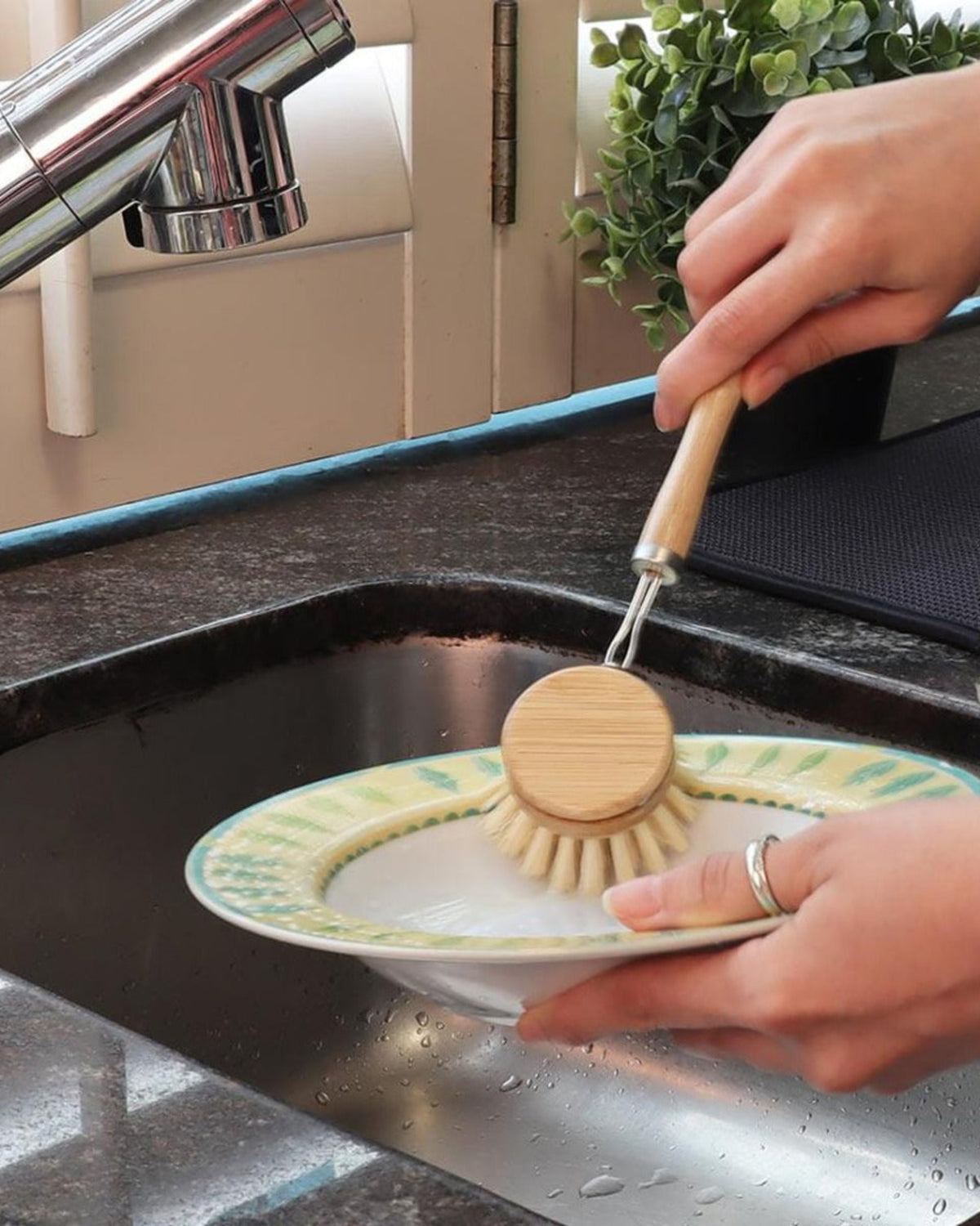 Person washing a plate with a wooden dish brush in a kitchen sink.