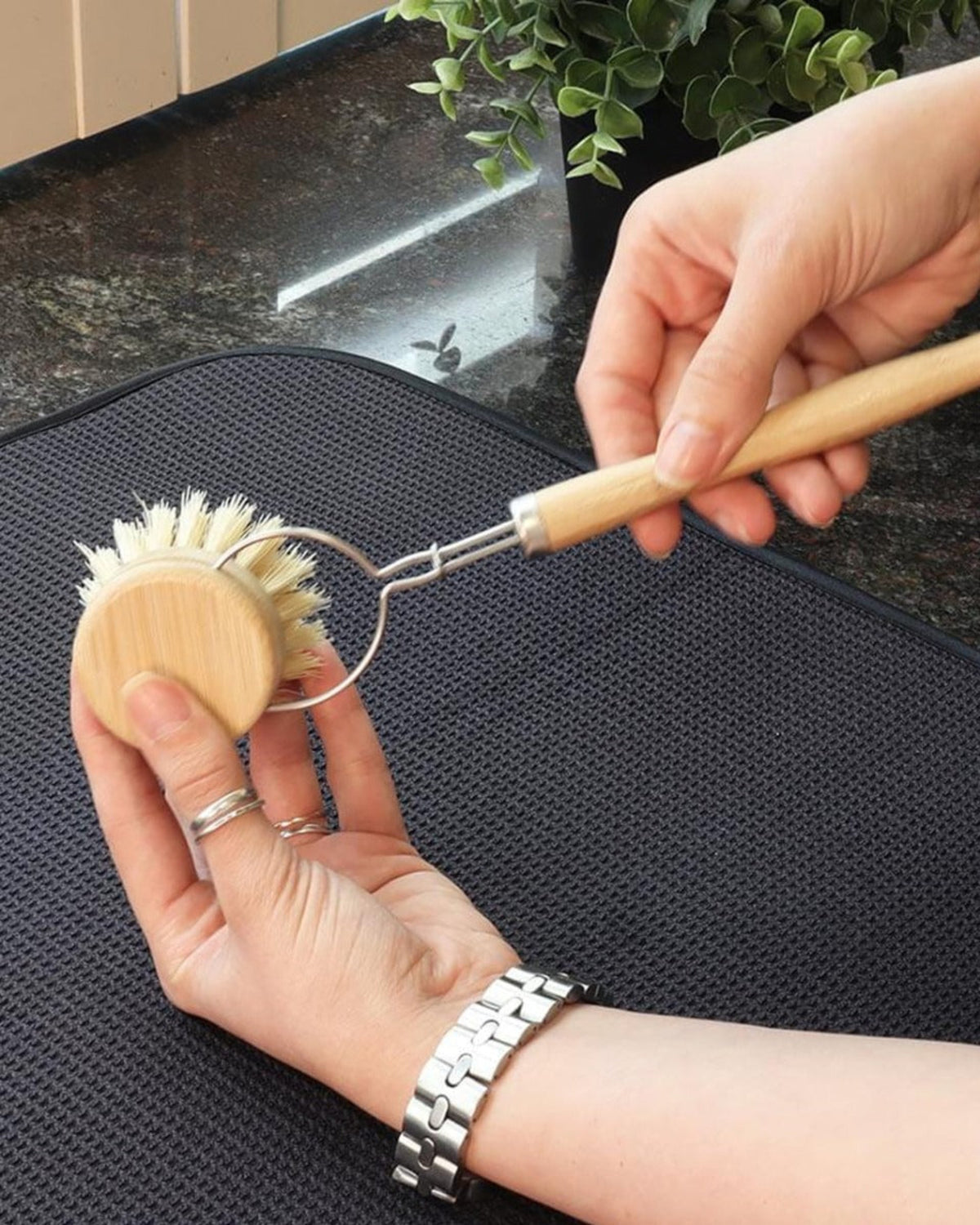 Person holding a wooden dish brush and a metal scrubber on a dark surface.