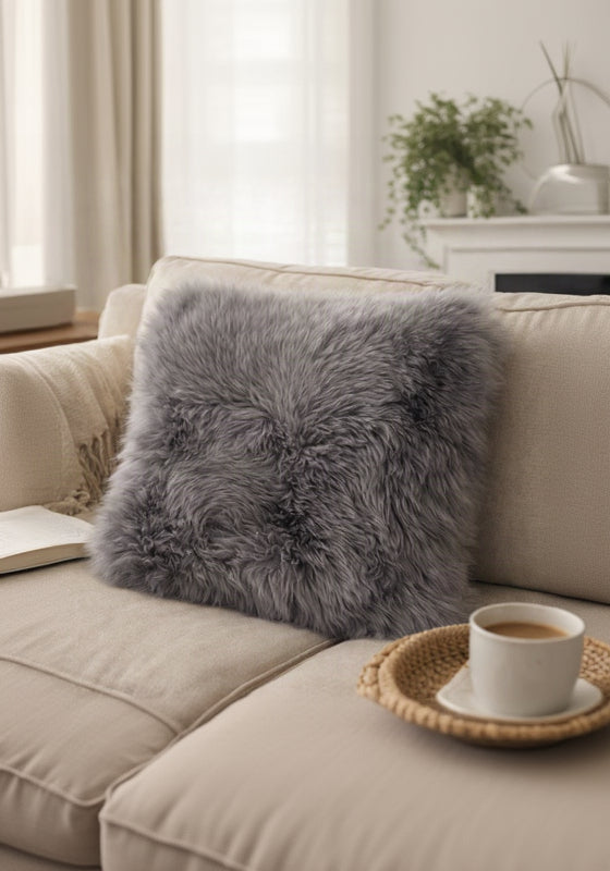 Gray fluffy pillow on a beige sofa with a book and coffee cup in a cozy living room.