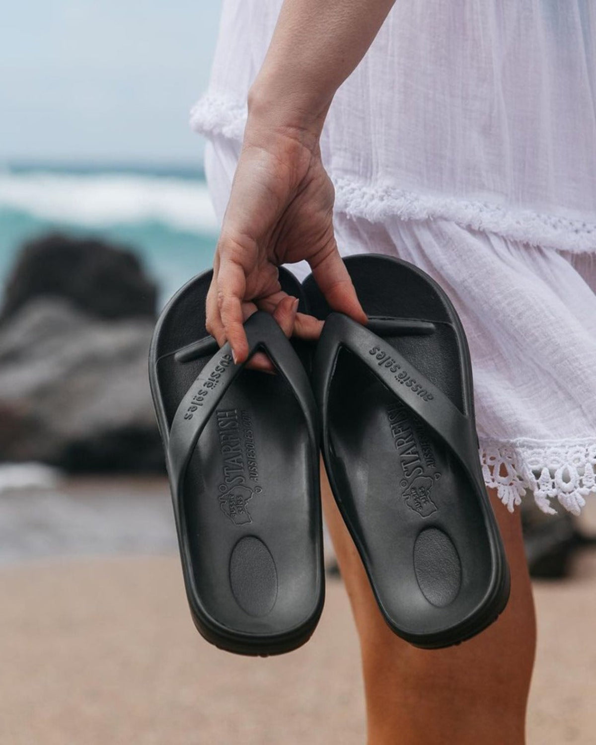 Jandals Person holding black  with a blurred beach background